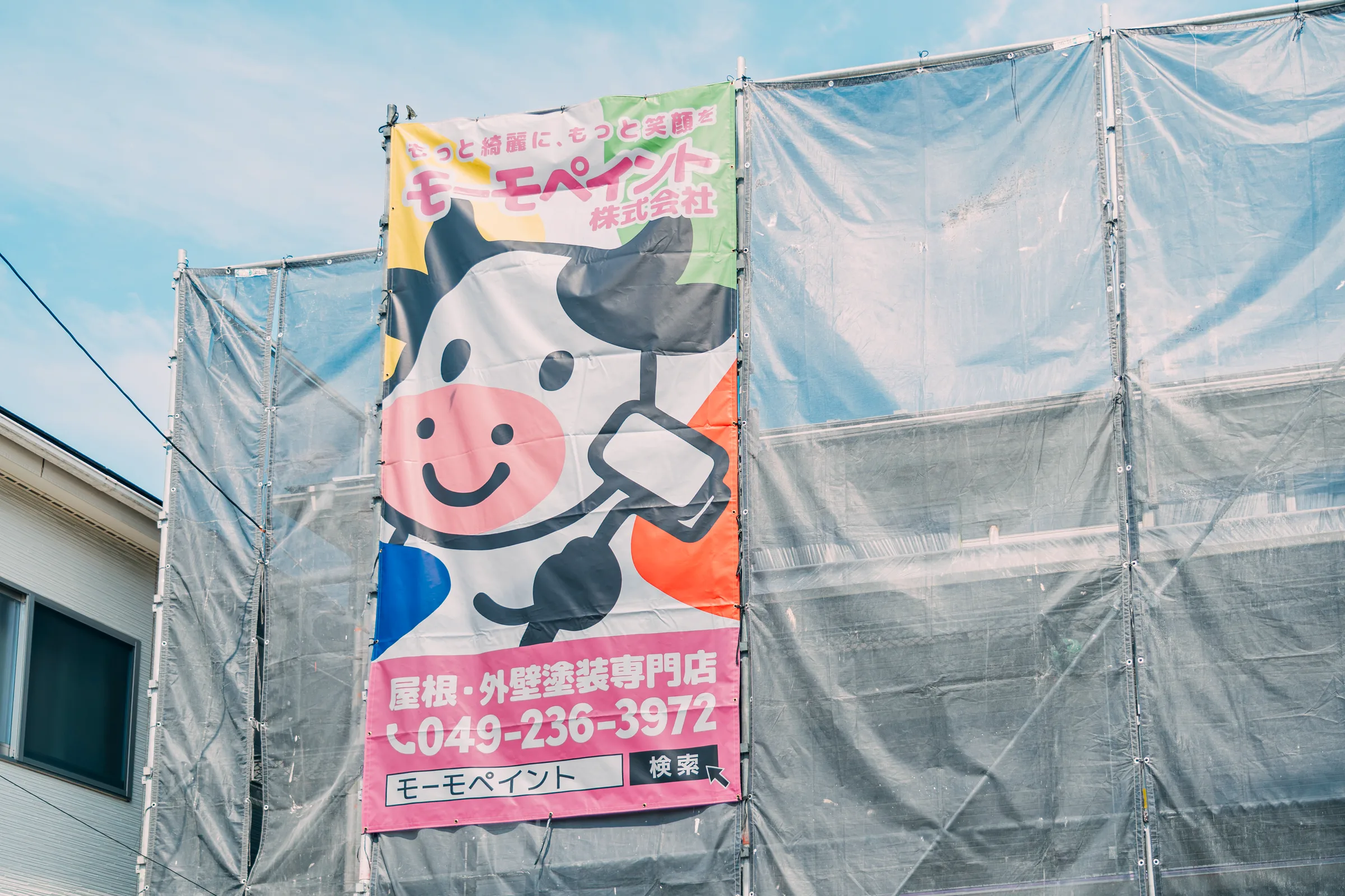 足場に掛けた現場シート（モーモペイントの看板）
