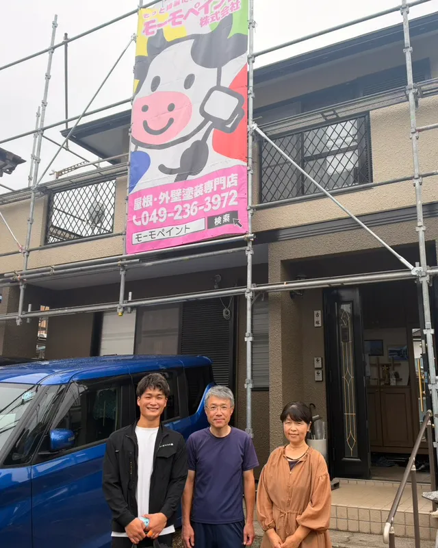 足場とモーモペイントの看板の前に並ぶお客様ご夫婦とスタッフ